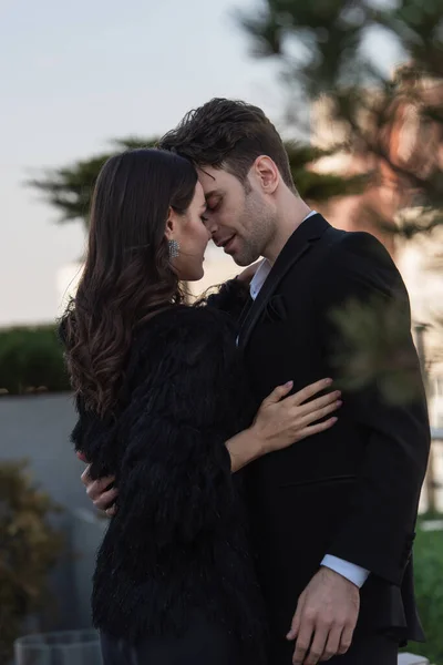 Eleganter Mann und Frau in Kunstpelzjacke umarmen sich vor blauem Himmel — Stockfoto