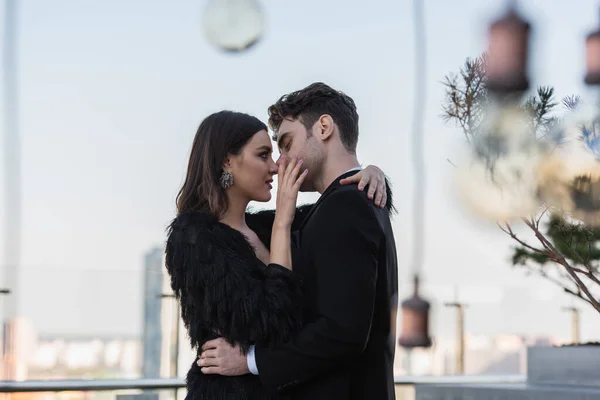 Woman in faux fur jacket touch face and embracing man in suit outdoors — Stock Photo