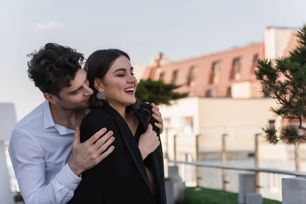 Mann umarmt fröhliche Frau im schwarzen Blazer auf Terrasse — Stockfoto