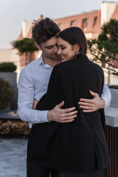 Alegre hombre abrazando feliz novia en negro chaqueta - foto de stock