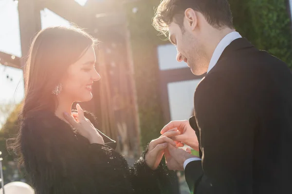 Hombre usando el anillo en el dedo de la novia feliz al aire libre - foto de stock