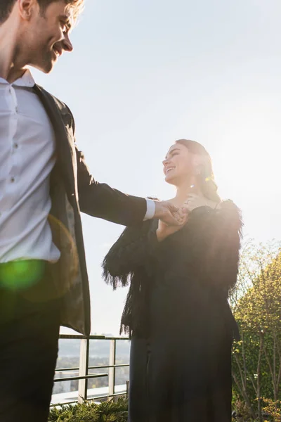 Hombre de traje y mujer feliz tomados de la mano en la terraza - foto de stock