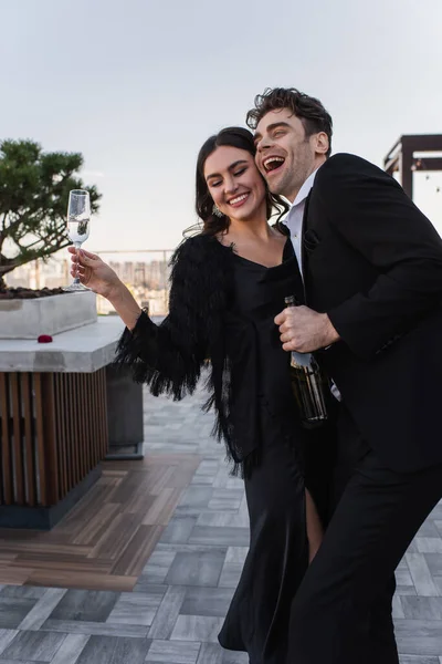 Uomo gioioso che tiene la bottiglia vicino a ragazza allegra con bicchiere di champagne — Foto stock