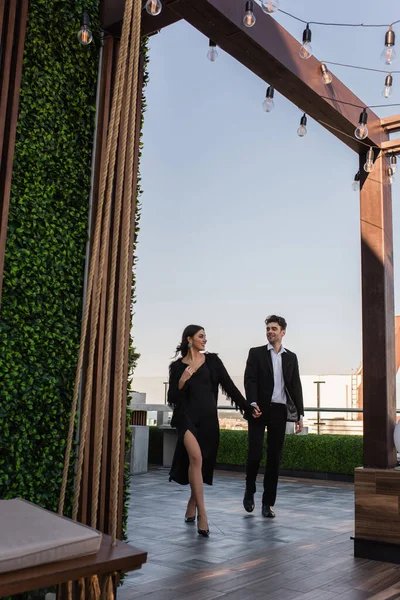 Повна довжина елегантної пари тримає руки під час прогулянки на терасі — стокове фото