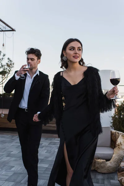 Donna felice che si tiene per mano con l'uomo che beve vino mentre cammina sulla terrazza — Foto stock