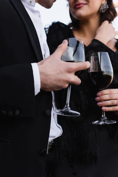 Vista recortada de elegante pareja sosteniendo copas de vino tinto - foto de stock
