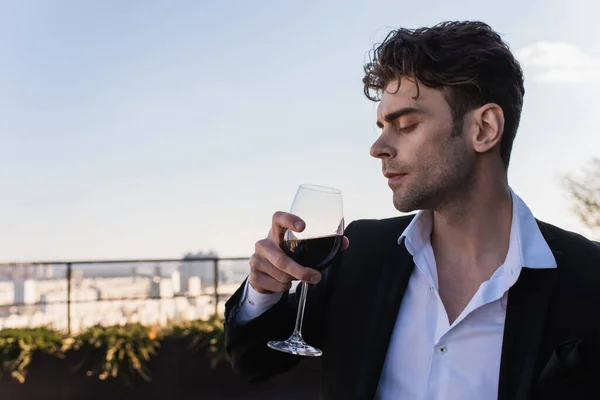 Élégant homme en costume tenant verre de vin rouge à l'extérieur — Photo de stock