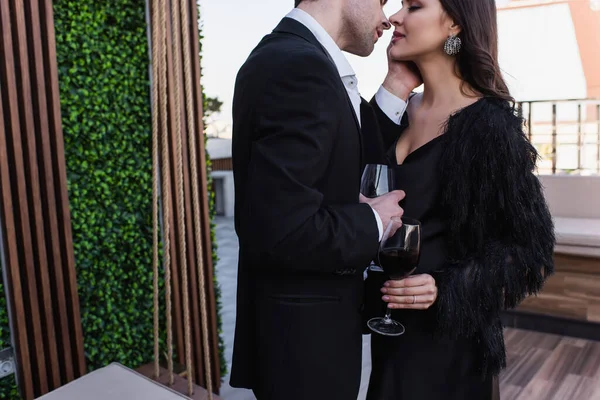 Homem beijando mulher e segurando copo de vinho tinto no terraço — Fotografia de Stock