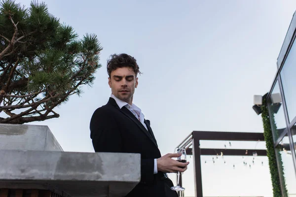 Good-looking man in suit holding glass of red wine on terrace — Stock Photo