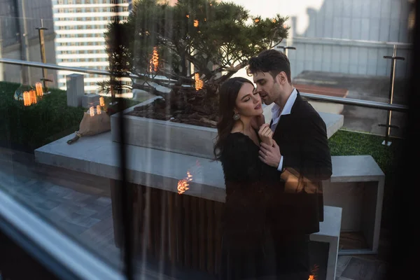 Woman and man hugging on terrace behind blurred window of restaurant — Stock Photo