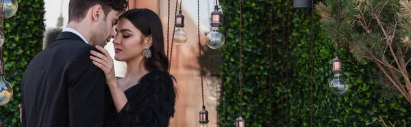 Elegant woman hugging man near light bulbs on terrace, banner — Stock Photo