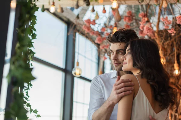 Hombre y mujer sonriendo mientras miran hacia otro lado y abrazándose en el restaurante — Stock Photo