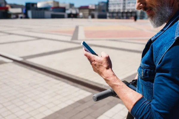 Ausgeschnittene Ansicht eines lächelnden bärtigen Mannes, der sein Smartphone mit leerem Bildschirm draußen hält — Stockfoto