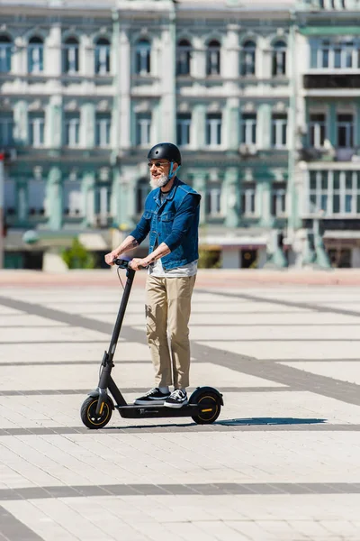 Full length of cheerful man in sunglasses and helmet riding e-scooter in urban city — Photo de stock