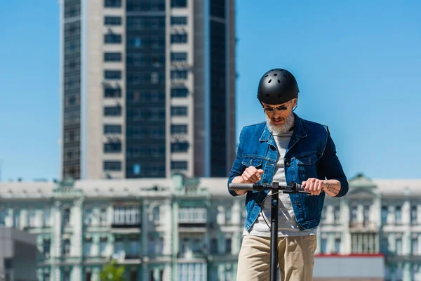 Middle aged man in sunglasses and helmet riding e-scooter in urban city — Photo de stock