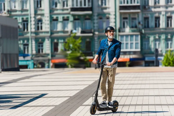 Full length of middle aged man in helmet riding e-scooter in urban city — Fotografia de Stock