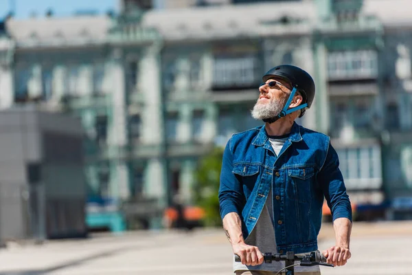 Positive man in sunglasses and helmet riding e-scooter in urban city — Foto stock