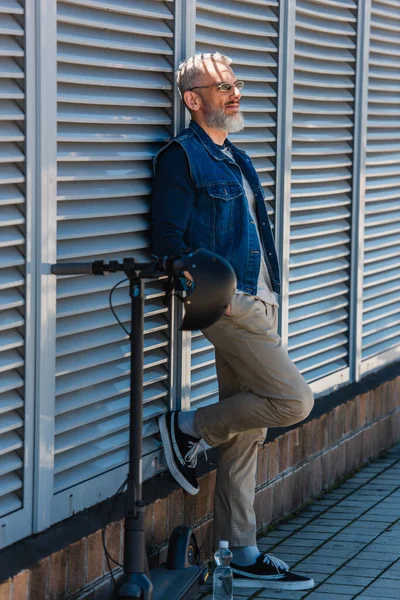 Bärtiger Mann mittleren Alters mit Sonnenbrille lächelt in der Nähe von Elektroroller — Stockfoto