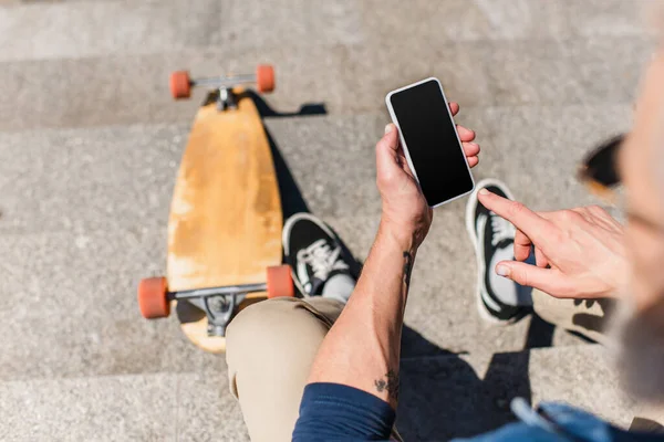 Top view of tattooed mature man using smartphone with blank screen near longboard on stairs - foto de stock