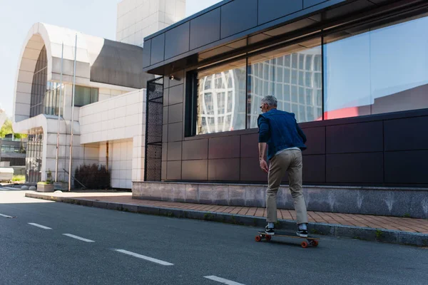 Back view of mature man riding longboard on urban street — Stock Photo