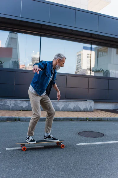 Full length of amazed and mature man riding longboard on urban street - foto de stock