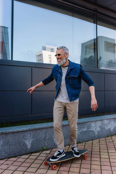 Full length of cheerful and mature man riding longboard on urban street — Stock Photo