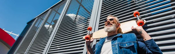 Low angle view of positive and middle aged man holding longboard on street, banner — Stock Photo