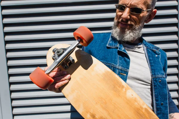 Smiling and middle aged man in sunglasses holding longboard — Fotografia de Stock