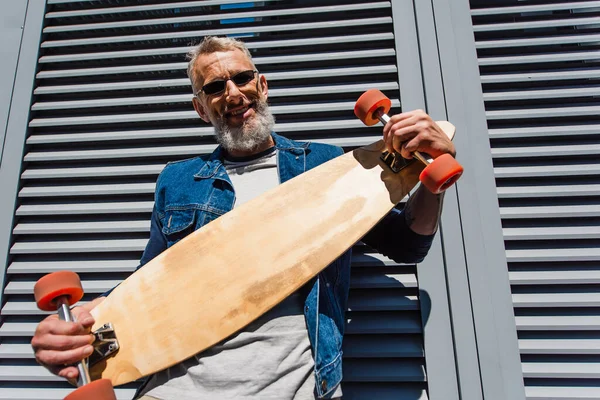 Pleased middle aged man in sunglasses holding longboard - foto de stock