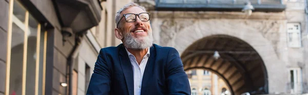 Happy bearded man in glasses looking up on urban street, banner — Photo de stock