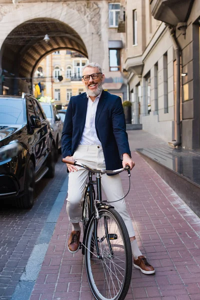 Glücklicher bärtiger Mann mit Brille fährt Fahrrad auf der Stadtstraße — Stockfoto