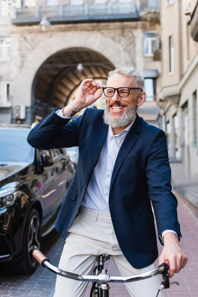 Happy bearded man adjusting glasses and riding bicycle on urban street — Foto stock