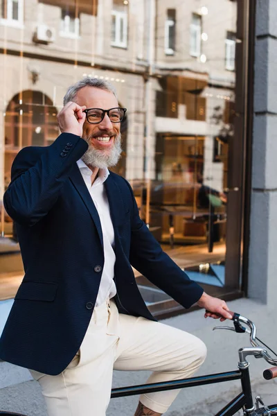 Happy bearded man adjusting glasses and riding bicycle on street — Foto stock