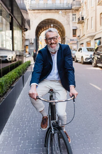 Щасливий чоловік середнього віку в окулярах верхи на велосипеді на сучасній міській вулиці — стокове фото