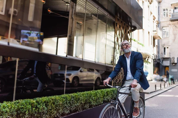 Glücklicher Mann mittleren Alters in Blazer und Brille, der auf modernen urbanen Straßen Fahrrad fährt — Stockfoto