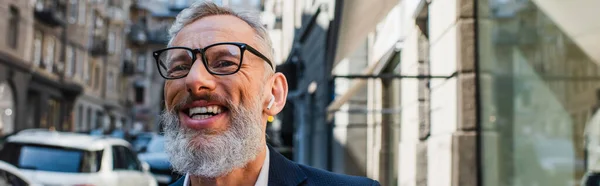 Glücklicher bärtiger Mann mit Brille und Kopfhörer auf urbaner Straße, Banner — Stockfoto