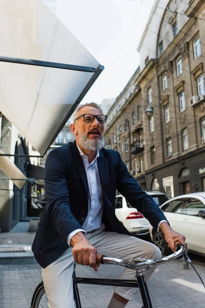 Mature man listening music in earphones and riding bicycle — Photo de stock