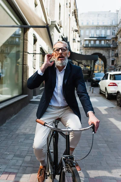 Happy mature man listening music and adjusting earphones while riding bicycle — Stock Photo