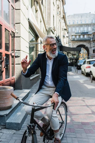 Positive mature man listening music in earphones and riding bicycle — Stock Photo