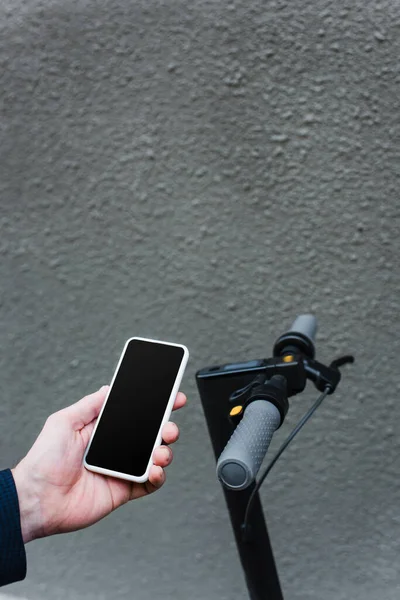 Teilansicht eines gestandenen Geschäftsmannes mit Smartphone mit leerem Bildschirm in der Nähe von E-Scooter — Stockfoto