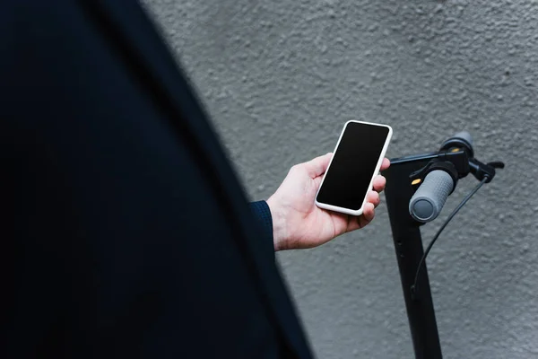 Частковий вид зрілого чоловіка, що тримає смартфон з порожнім екраном біля електронного скутера — стокове фото