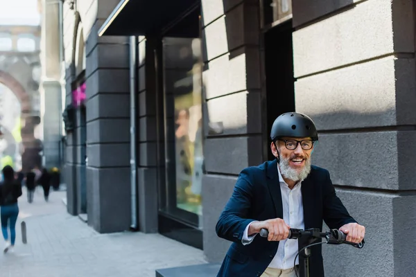 Joyful mature businessman in blazer and helmet riding e-scooter — Stock Photo