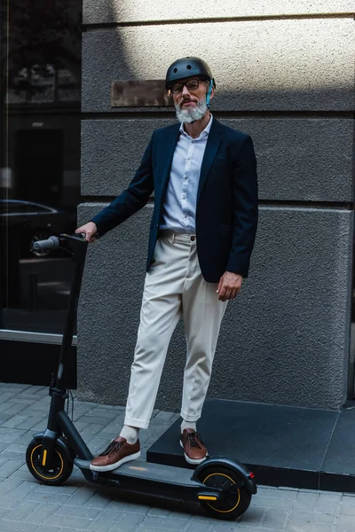 Full length of middle aged businessman in blazer and helmet near e-scooter - foto de stock