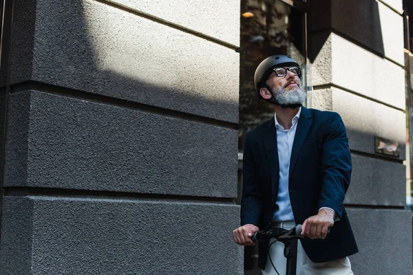 Mature businessman in blazer and helmet riding electric scooter — Fotografia de Stock