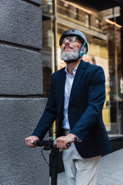 Pleased mature businessman in blazer and helmet riding electric scooter and looking up — Foto stock