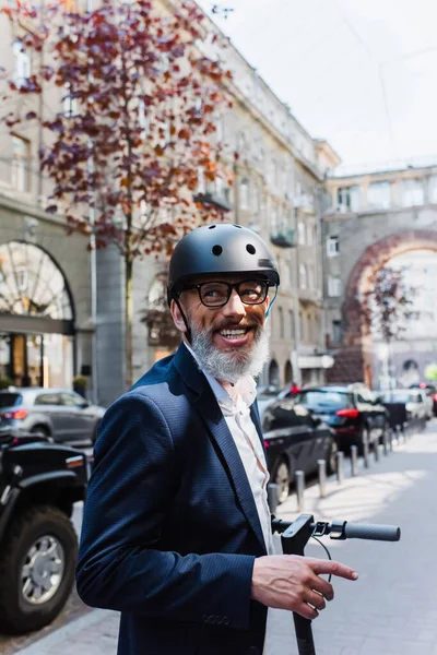 Joyful and mature businessman in blazer and helmet riding electric scooter — Stock Photo