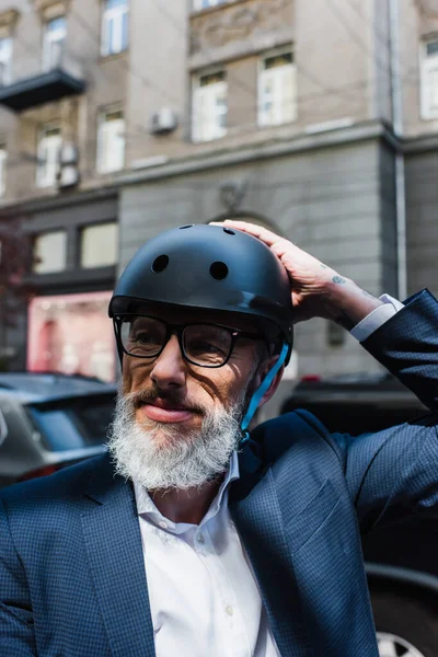 Mature businessman in blazer adjusting helmet outside — Stock Photo