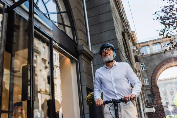 Low angle view of mature man in shirt and helmet riding electric scooter — Photo de stock