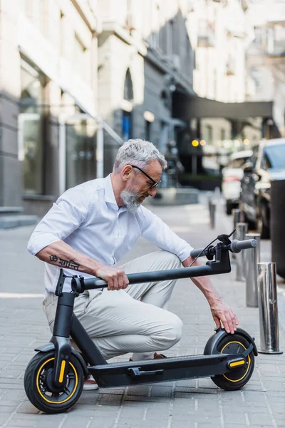 Mature man adjusting electric scooter on street — Stock Photo