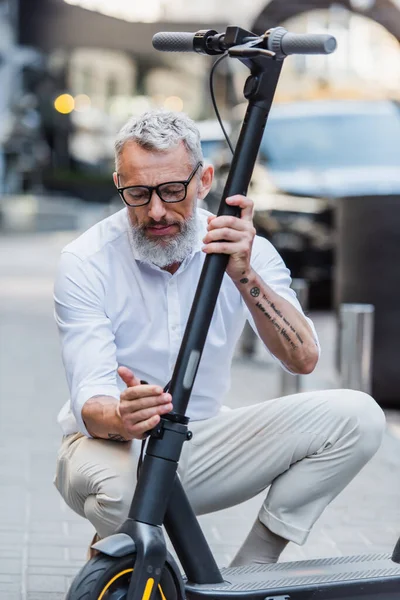 Зрелый мужчина в очках регулирует электрический скутер на улице — стоковое фото